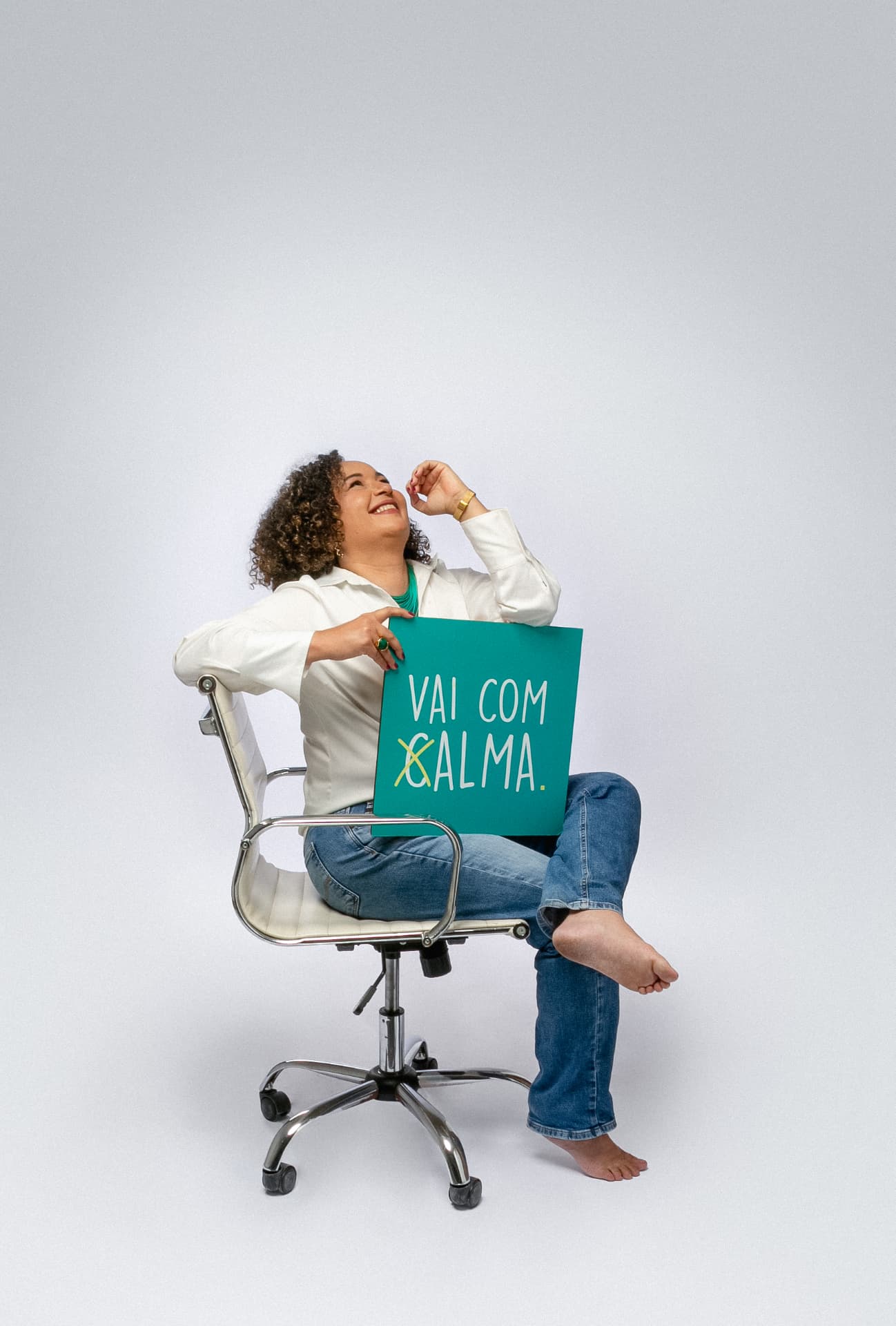 Kelly Metzker sentada em uma cadeira de escritório segurando uma placa com a frase Vai com calma